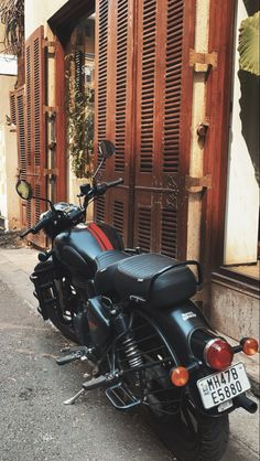 a black motorcycle parked on the side of a street next to a building with shutters