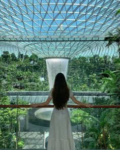 a woman in a white dress standing on a balcony looking out at the trees and greenery