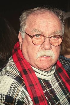 an older man with glasses and a red scarf is looking off to the side while standing in