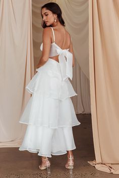 a woman wearing a white dress and high heels standing in front of curtained curtains