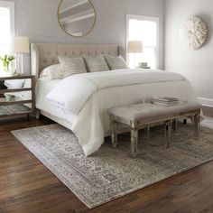 a white bed sitting on top of a wooden floor next to a mirror and lamp