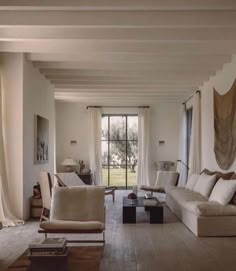 a living room filled with lots of furniture next to a large open window covered in curtains