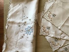 some white linens with embroidered designs on them and one has a flower in the middle