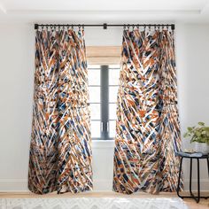 a living room with white walls and wooden flooring, two windows covered in patterned curtains