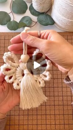 two hands are holding an ornament made out of yarn and beads on a table