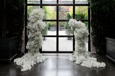 two sculptures made out of white flowers in front of an open window with a brick wall