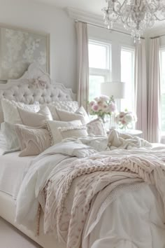 a white bed sitting in a bedroom next to a window filled with curtains and pillows