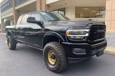 a black ram truck parked in front of a building with large tires on it's tires