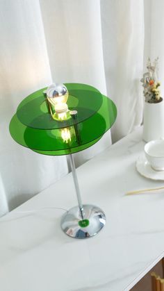 a green table lamp sitting on top of a white counter next to a cup and saucer