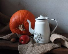 a white tea pot sitting on top of a wooden table next to an apple and a pumpkin