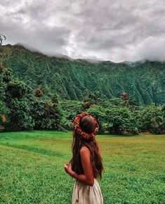 a girl standing in the middle of a lush green field with mountains in the background