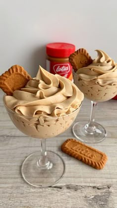 two glasses filled with dessert on top of a wooden table next to crackers and a can