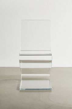 a clear chair sitting on top of a cement floor next to a white wall and two shelves