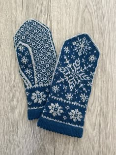 a pair of blue mittens sitting on top of a wooden floor with snowflakes