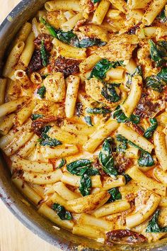 a pan filled with pasta and spinach on top of a wooden table next to utensils