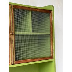 a green shelf with a wooden frame and mesh on the top, in front of a white wall