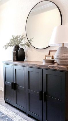 a black sideboard with two vases and a round mirror on the wall above it