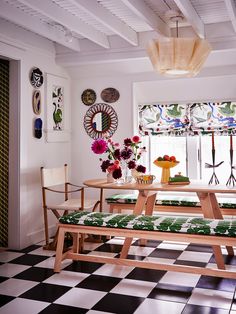 a room with checkered flooring and wooden benches in front of the window, decorated with flowers