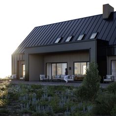 a person walking in front of a house with a black metal roof and large windows