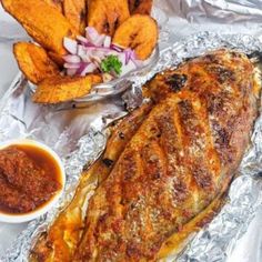 an image of fish on tin foil with sauces and french fries in the background