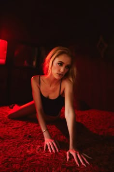 a woman laying on top of a bed in a dark room with red light coming from behind her