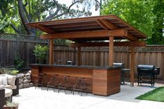 an outdoor bar in the middle of a backyard with seating around it and a grill area