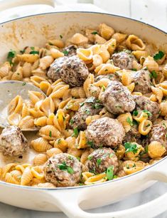 a skillet filled with pasta and meatballs on top of a marble countertop