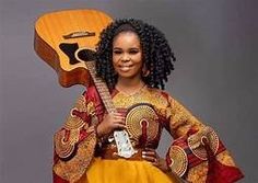 a woman in an african dress holding a guitar and posing for the camera with her hands on her hips