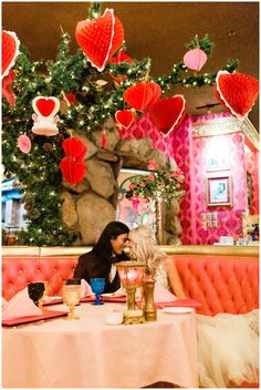 two women sitting at a table with red hearts hanging from the ceiling and decorations above them