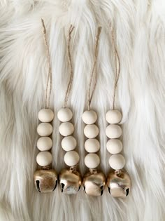 three wooden bells are hanging on a white fur covered surface with gold and silver beads