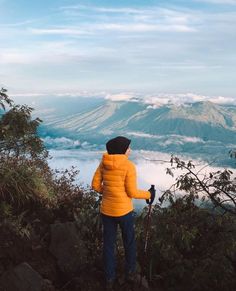 a person standing at the top of a mountain looking out over some clouds and mountains