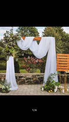 an outdoor wedding setup with white drapes and greenery on the side, surrounded by stone walls