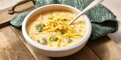 a bowl of broccoli cheese soup on a cutting board with a green napkin