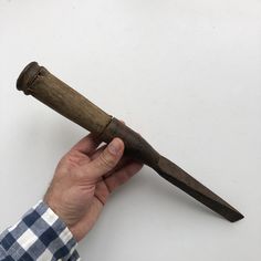 a person holding an old wooden knife in their hand on a white surface with a checkered shirt