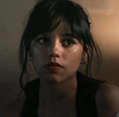 a close up of a person with dark hair and piercings on her ear, wearing a black top