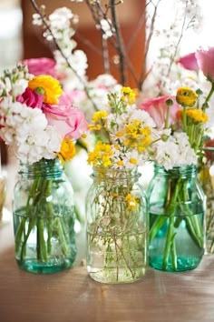 three mason jars with flowers in them sitting on a table next to other vases