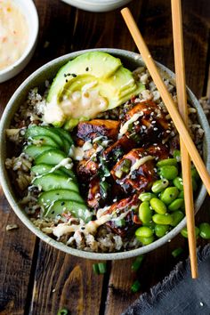 a bowl filled with rice and vegetables next to chopsticks on a wooden table