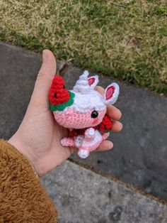 a small crocheted stuffed animal is held in someone's hand on the sidewalk