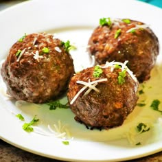 three meatballs on a plate with parsley sprinkled around them and garnished with shredded parsley