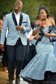 a man and woman in formal wear walking down the street with other people behind them