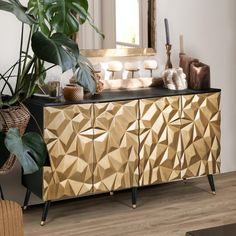 a gold and black sideboard next to a plant in a living room with white walls