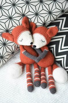 two knitted foxes cuddling on top of each other in front of a black and white background