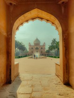 an archway leading to a large building with a fountain in the middle and palm trees on either side