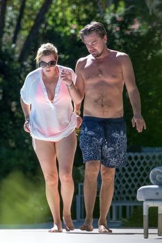 a shirtless man and woman walking down the street with one holding a cell phone