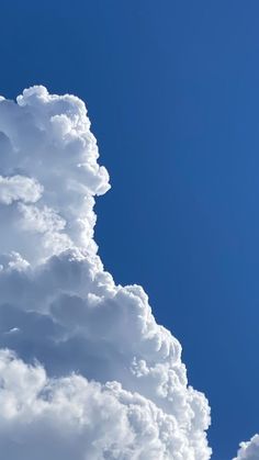 the plane is flying high in the blue sky with white clouds behind it on a sunny day