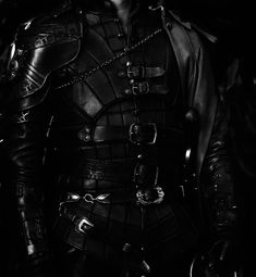 black and white photograph of a man in leather armor with chains on his chest, looking to the side