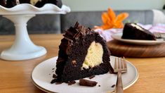 a piece of chocolate cake on a plate with a fork next to it and the rest of the cake in the background