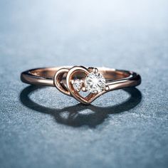 a heart shaped ring with a single diamond in the center on a blue table top