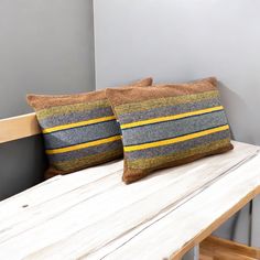 two striped pillows sitting on top of a wooden bench next to a white wall and wood floor