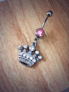 a pink jeweled crown belly ring on a wooden table